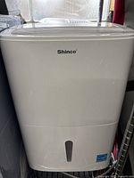 Front view of white Shinco dehumidifier showing brand and water level window.