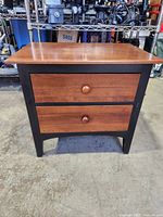 Front view of the wooden Ethan Allen nightstand showing two drawers with wooden knobs and black legs and frame.