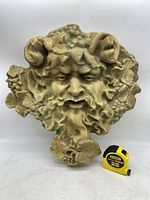 Front view of beige resin Green Man Bacchus wall sculpture with Stanley measuring tape placed beside for scale.