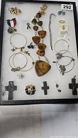 Displayed assortment of jewelry in a case with multiple items including stone necklace, hoop earrings, pins, crosses, and bracelets.