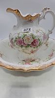 View of ornate porcelain pitcher with pink and white floral design and gold trim inside matching wash basin.