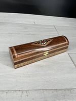 Photo showing angled front and top view of a wooden keepsake box with intricate inlaid patterns and brass clasp closure.