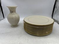 Photo of 12 Lenox Mansfield dinner plates stacked and Lenox beige porcelain vase beside them.