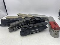 Grouped image showing several vintage Lionel metal train engines and passenger cars in black, silver, and red.