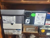 Photo showing stacked shoeboxes with sizes and brands including ECCO, FootJoy, Bass, and Dexter.