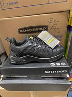 Single black safety shoe displayed on its box, showing sleek design and sturdy sole.