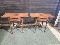 Pair of mahogany drop leaf side tables with visible water stains and surface wear on tabletops, shown with leaves extended.