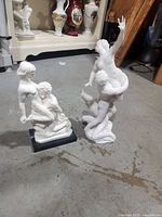 Two white marble-style statues on a gray floor showing size and detail, one with a black marble base.