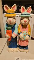 Front view of the two paper mache bunnies showing their faces and front details such as the carrot and decorated egg held.