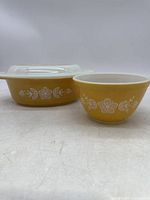 Side view of two yellow Pyrex bowls with white floral pattern, one with lid