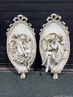 Pair of Renaissance-style plastic resin cameo wall plaques showing full front view against a dark background, both oval with raised detailed figures.