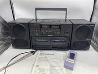 Front overview of Sony stereo system with two Mega Bass speakers, remote control in box, and instructions laid out