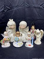 Seven angel figurines arranged on black background, showing entire collection including two large white ceramic angels and smaller month angels.