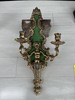Full view of the ornate cast metal wall sconce with green felt backing and two candle holders.