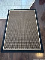 Full view of rectangular area rug on floor showing overall size and color with black border and brown patterned center.