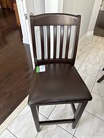 Front view of the wooden bar stool with leather-like padded seat and slatted backrest.