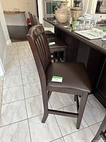 Side view of dark wood bar stool with brown padded seat and curved slatted backrest, situated in kitchen area.
