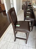Wooden bar stools lined up by kitchen counter, visible brown leather-like seats and vertical slat backs.