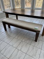 Front right perspective view of wooden bench under table on tiled floor
