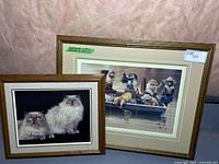 Photo shows both framed artworks leaning against a wall: larger 'Gone Fishing' print behind and a smaller Persian cat print in front, both with wood tone frames.