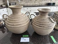 Two beige clay pots with ring handles, one 12 inches tall and one 11 inches tall, displayed on a kitchen counter.
