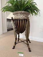 Full view of the decorative stand planter with artificial fern showing the woven basket and leaf motif legs.