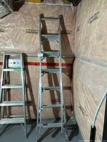 Front view of the aluminum ladder extended to different heights placed against an insulated basement wall.