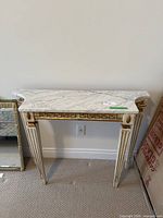 Full view of marble top hall table against wall showing marble surface, ornate carved legs with gold accents.