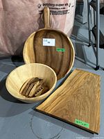 Photo showing all items in lot: round wooden serving tray with handle and hanging rope, round wooden salad bowl with wooden utensils inside, and rectangular cutting board.