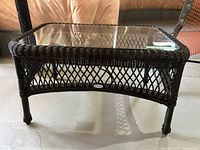 Full view of the dark brown wicker outdoor table with glass top on a concrete floor.