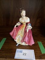 Front view of Royal Doulton Southern Belle figurine standing on a wooden surface with a lot number card.