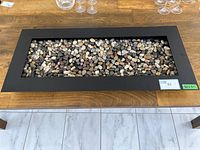 Photo showing a rectangular metal frame table top decor filled with decorative stones of various colors and sizes.