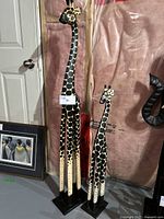 Full view of two tall wooden giraffe sculptures with natural wood finish and black and white giraffe spot patterns, standing on black bases.