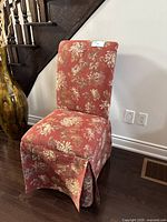 Photo of the upholstered accent chair showing the front and side view with floral fabric covering the high back and skirted base.