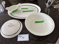 Wide view of all items in set including serving bowl with lid, oval platter, and gravy boat on black surface with green tape labels for size.