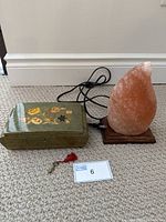 Music box and salt lamp displayed together on carpeted floor, showing music box top with floral marquetry and salt lamp natural pink-orange color with cord.