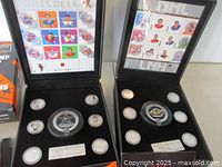 Two open black display cases each containing multiple NHL silver-toned medallions arranged around a central larger medallion resembling a hockey puck with NHL logos, including accompanying sheets of stamps behind the lids showing players' portraits.