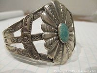 Front angle view on graph paper showing sunburst stamping with central oval turquoise