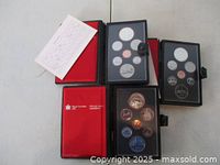 Four leatherette presentation cases open showing red interiors and coin trays with six base metal coins and a large commemorative silver dollar.