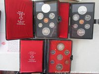 Three open black clamshell cases showing red velvet interiors with 1973, 1974 and 1975 coin sets