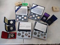 All four uncirculated coin sets in folders and five individual silver dollar coins laid out on table