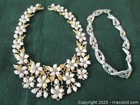 Both necklaces displayed on green fabric background, floral pearl necklace on left, silver choker on right