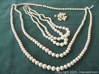 Two vintage pearl necklaces laid flat on dark green cloth with bag of 17 extra pearls visible