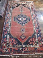 Front view of the entire rug laid on wooden floor showing central medallion, border and fringed edge.