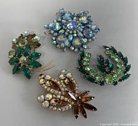 Top view of four vintage rhinestone brooches arranged together showing colors and design details.