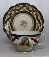 Antique teacup and saucer with front view showing woman portrait and detailed border design.