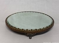 Front angle view of the antique Victorian footed plateau vanity mirror showing beveled mirrored top, decorative metal rim, and claw foot detail.