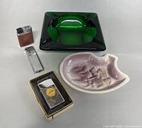 Overall lot including two vintage lighters, a boxed Zippo lighter and two ashtrays, one green glass and one ceramic purple-white.