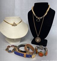 Full view of lot jewelry on white and black busts including 3 necklaces and stacked bracelets with various materials and colors.