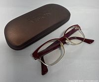 Eyeglasses resting outside the brown hard protective case on a white surface, showing full glasses and case.